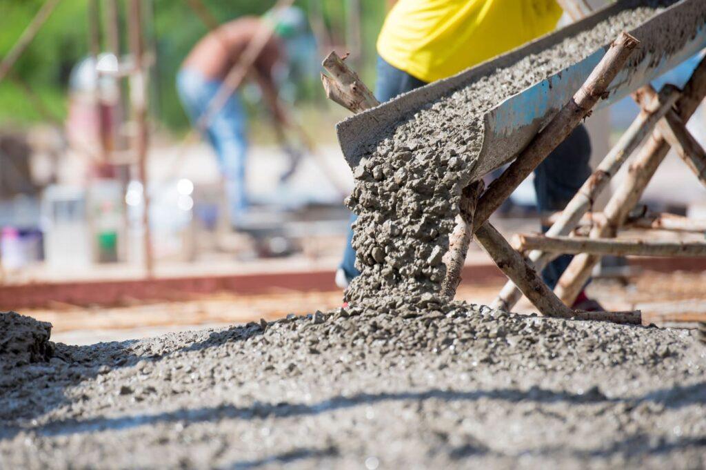 Arbeiter gießen frischen Beton aus einer Schubkarre auf eine Baustelle, ideal für den Bau langlebiger Betonzäune.