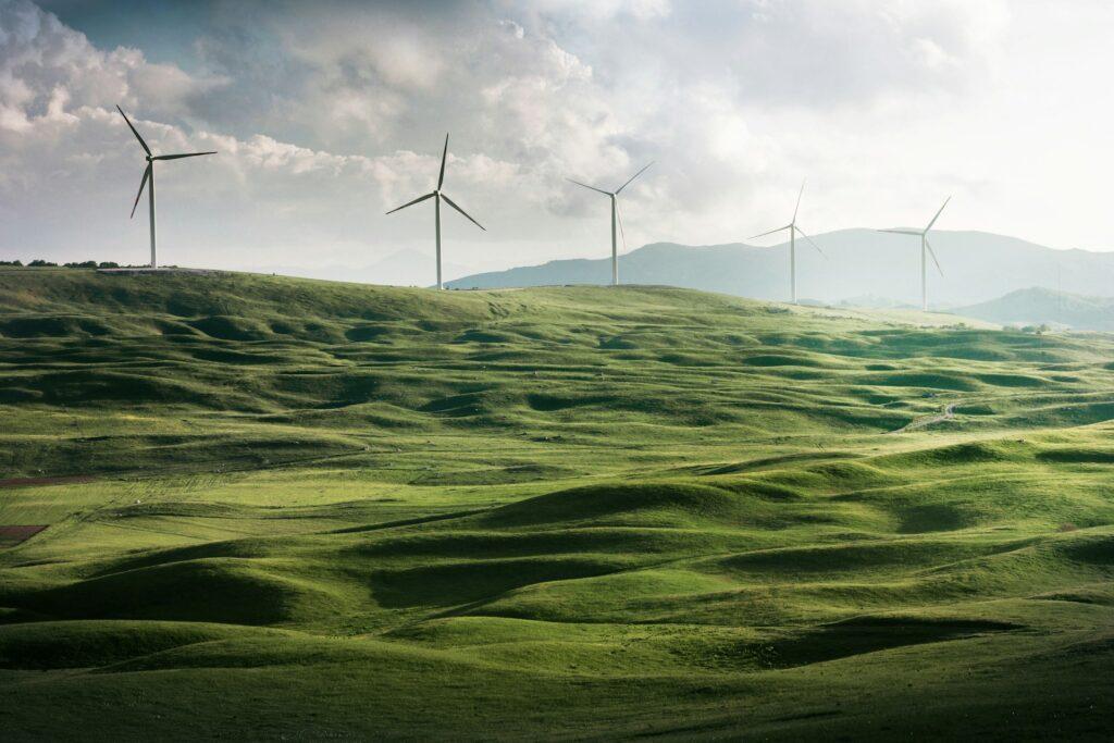 Windkraftanlagen auf grünen Hügeln bei bewölktem Himmel, die erneuerbare Energie erzeugen und zur nachhaltigen Energiegewinnung beitragen.