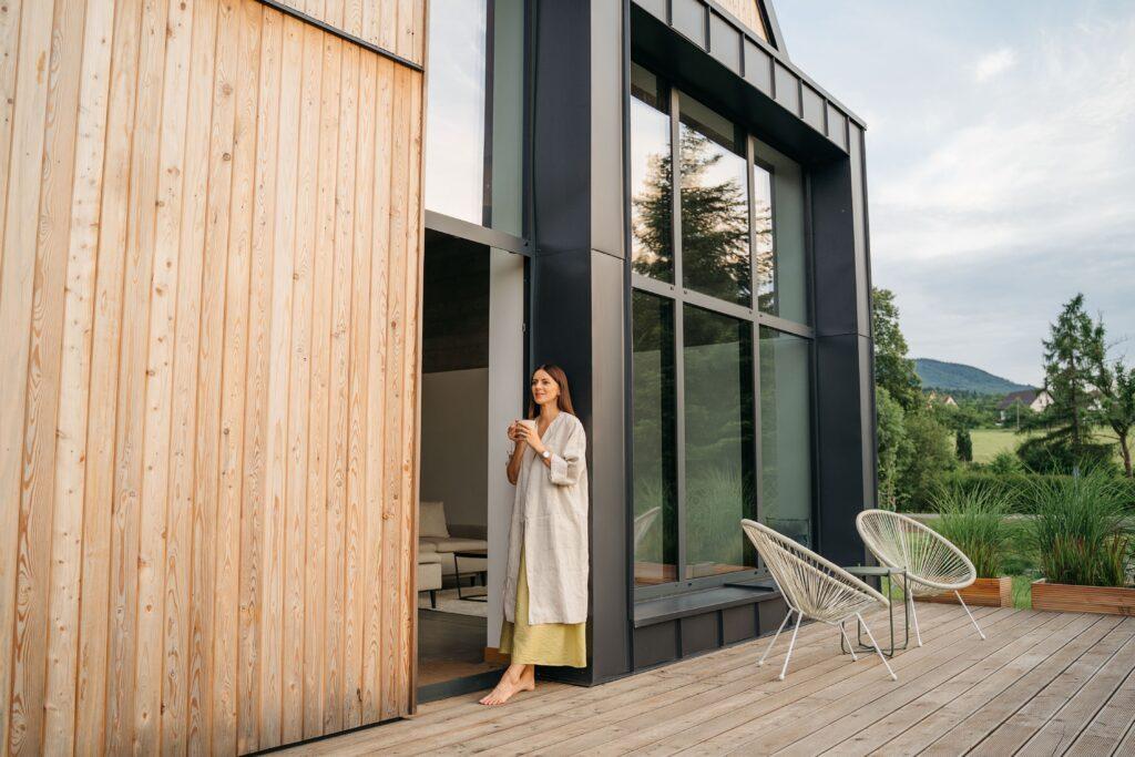 Eine Person steht angelehnt an ein Haus mit einem Getränk in der Hand