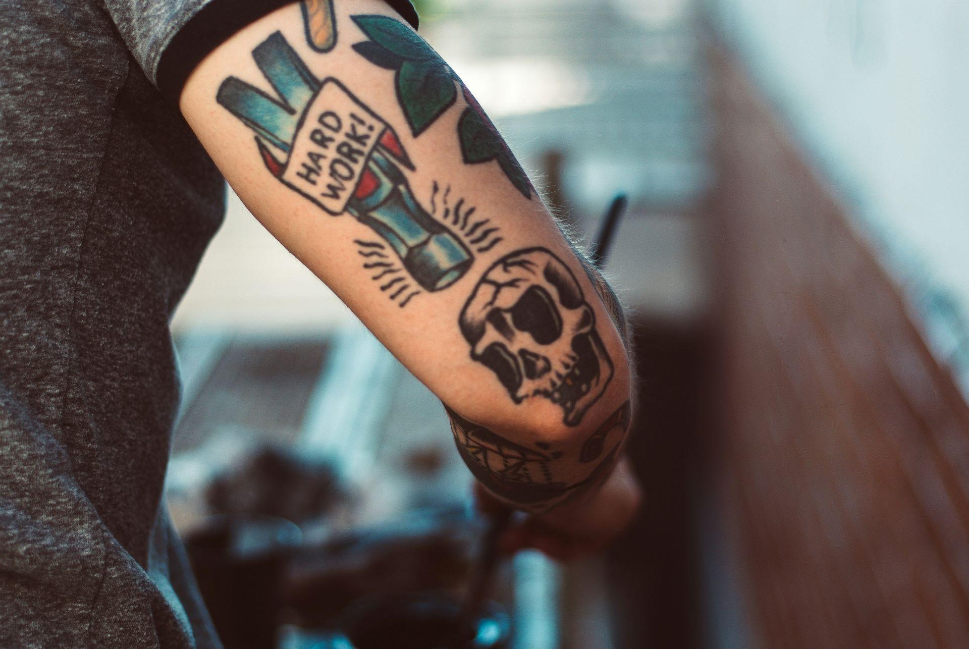 Tätowierter Arm mit Totenkopf und Hammer mit der Aufschrift „Hard Work“