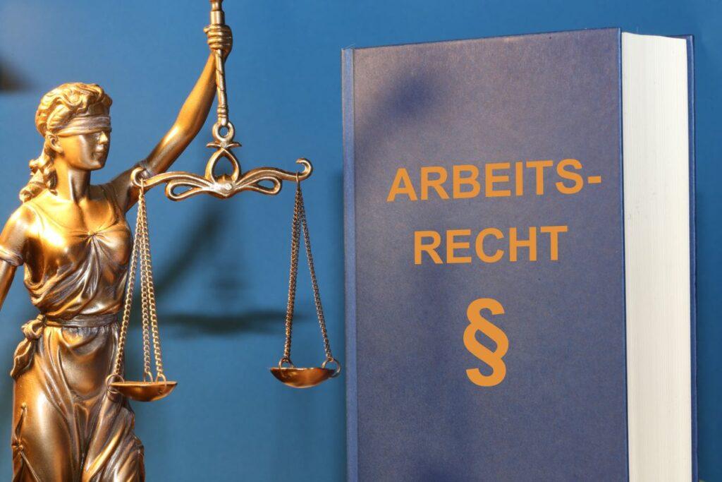 Ein Buch mit der Aufschrift „Arbeitsrecht“ und die Justitia-Statue als Symbol für einen Anwalt für Arbeitsrecht Mönchengladbach.