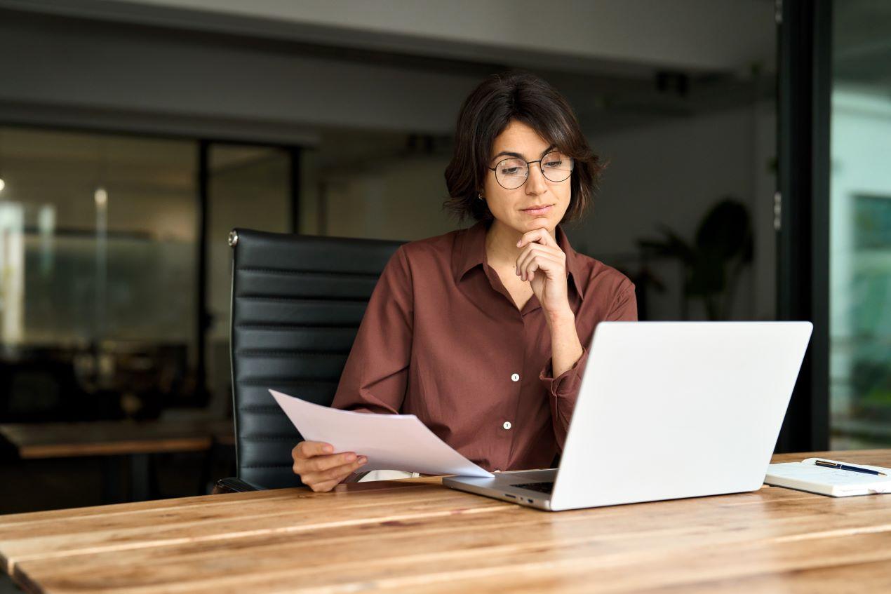 Eine Frau im Büro prüft Dokumente vor einem Laptop – ideal zur Vorbereitung auf ein Gespräch mit einem Anwalt für Arbeitsrecht Mönchengladbach.