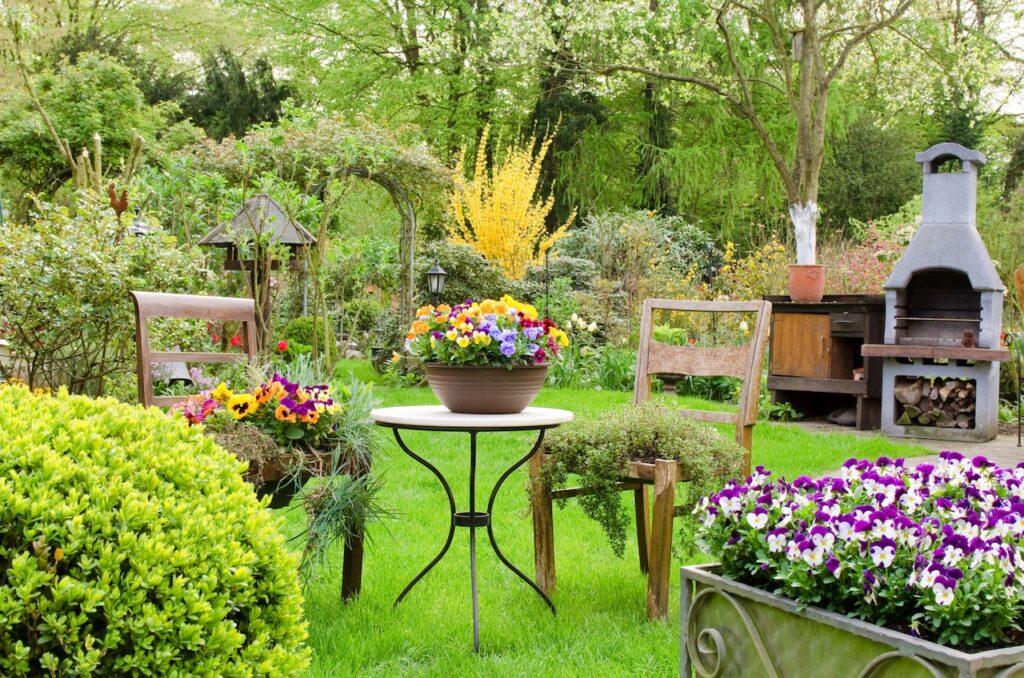 Blumenreicher Garten mit Sitzbereich, Grill und Dekoration im Fruehling 