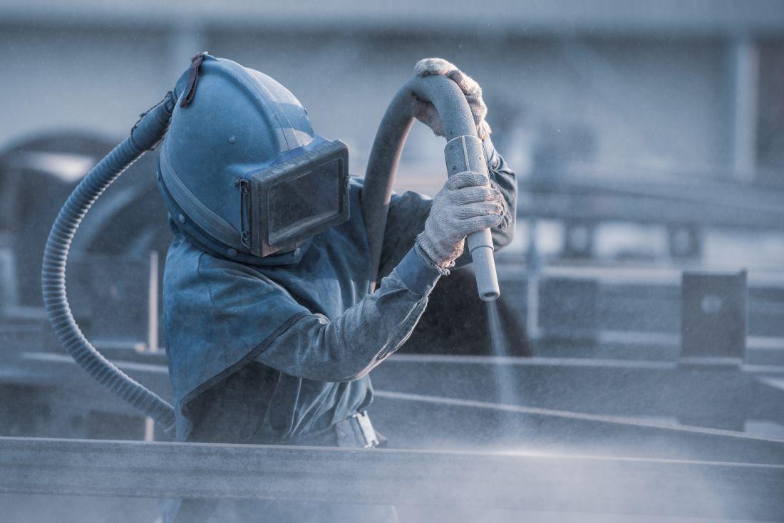 Sandstrahler mit Schutzanzug und Sandstrahlschlauch reinigt Metallkonstruktion im Außenbereich