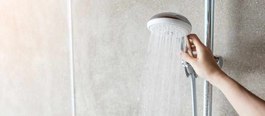 Hand regelt Wasserstrahl an moderner Handbrause vor Duschrueckwand Aluverbund in natuerlicher Steinoptik