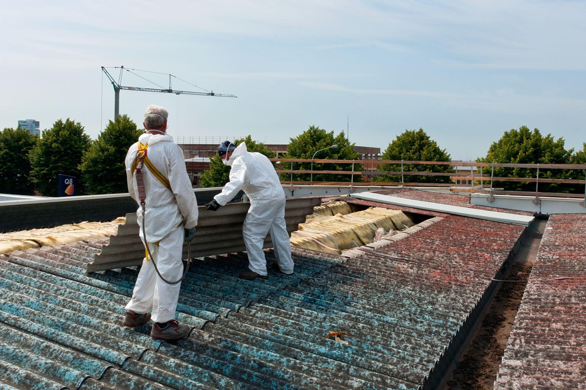 Arbeiter in Schutzanzügen entfernen Dachplatten