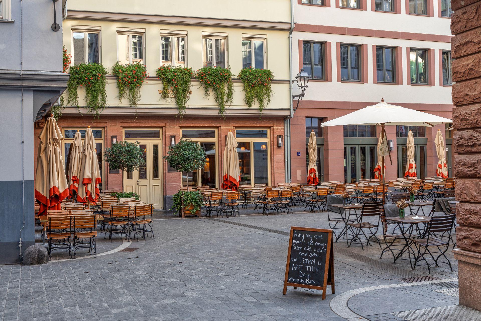 Gemuetlicher Platz mit Straßencafe in Frankfurts Altstadt mit Holzstuehlen und Schirmen vor hellen Fassaden