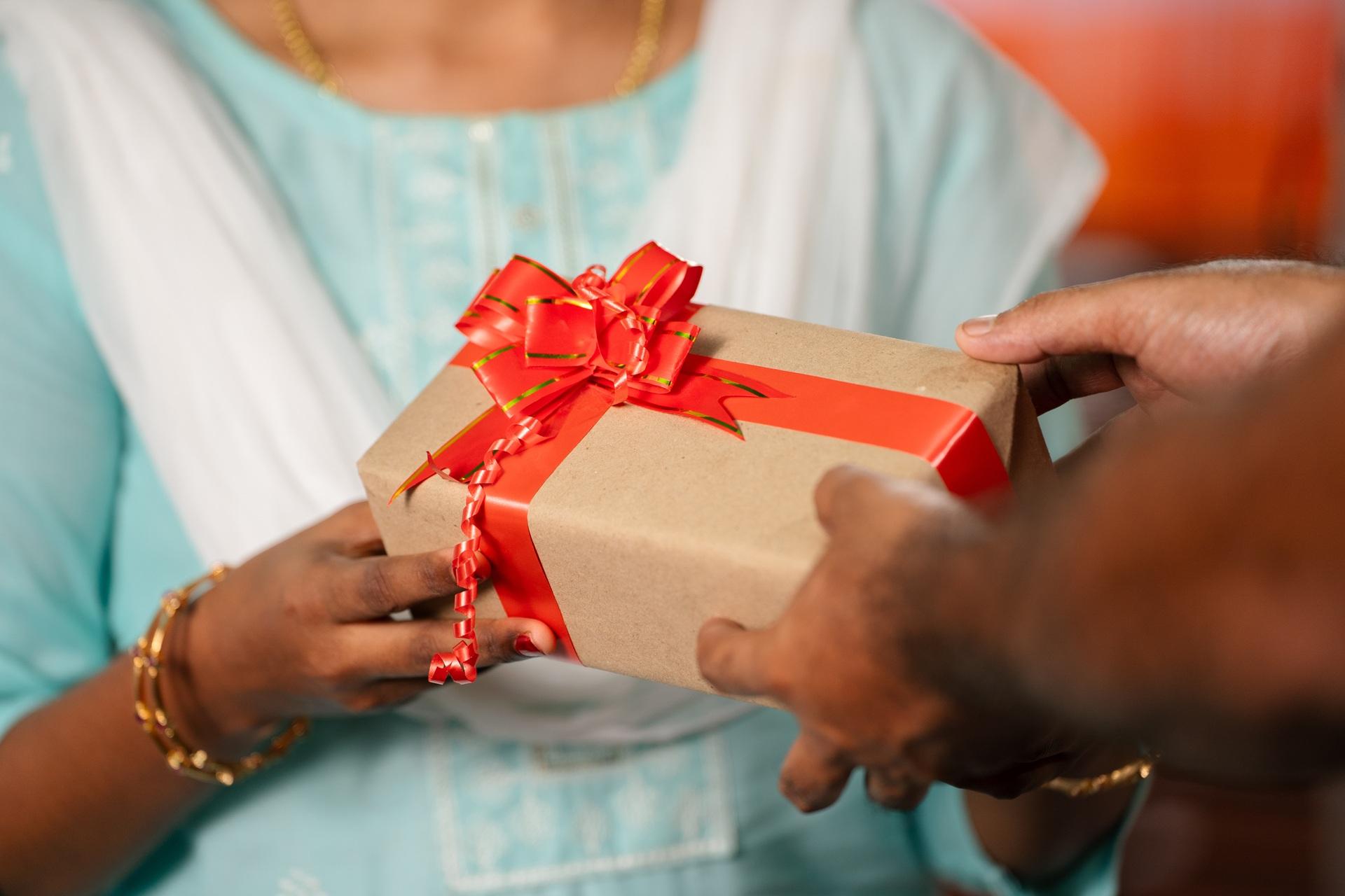 Geschenk mit roter Schleife ueberreicht | Kundengeschenke