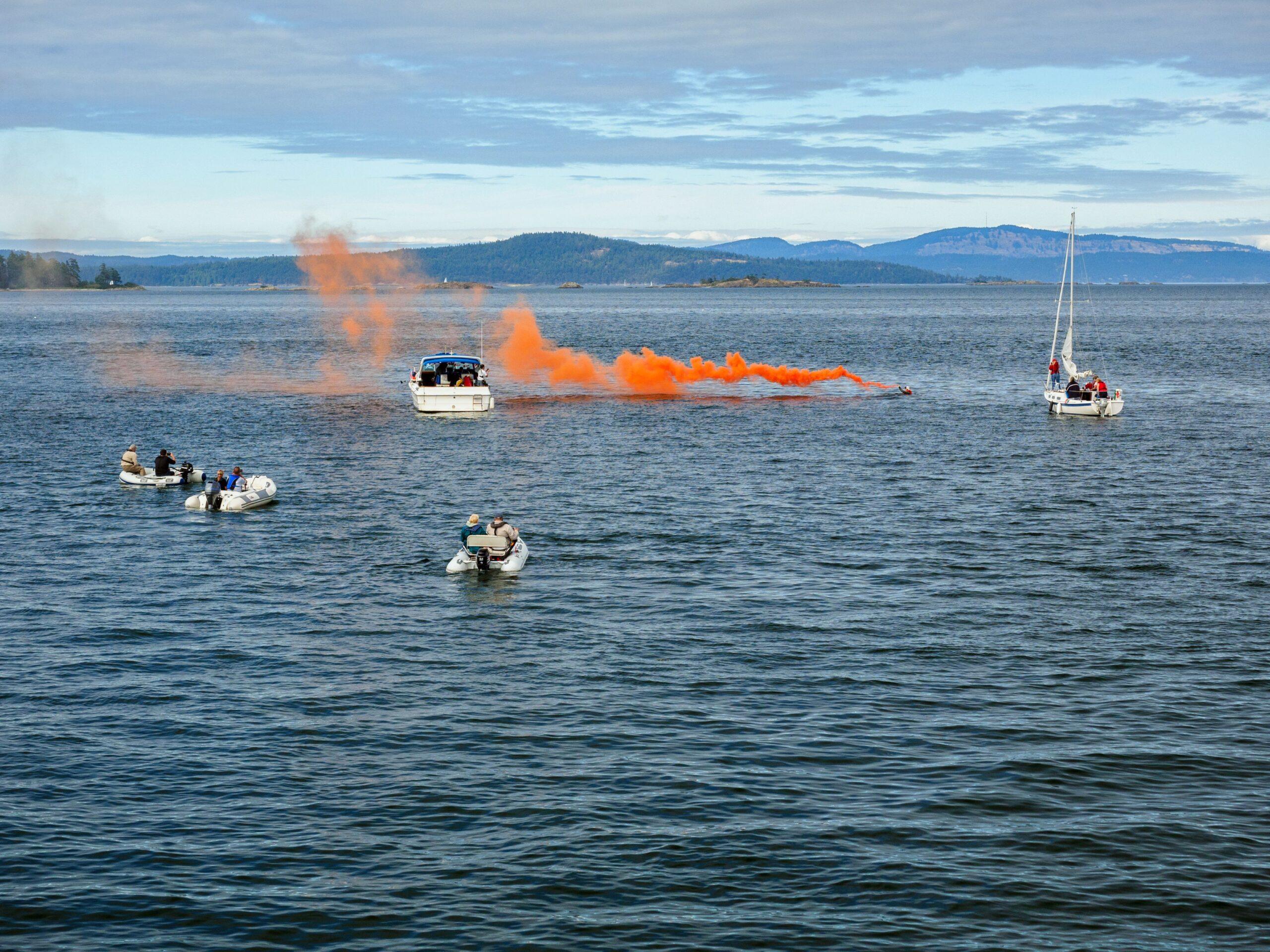 Boote orientieren sich an einer orangefarbenen Rauchspur, die als deutliches Signal durch Leuchtmunition auf dem Wasser eingesetzt wird